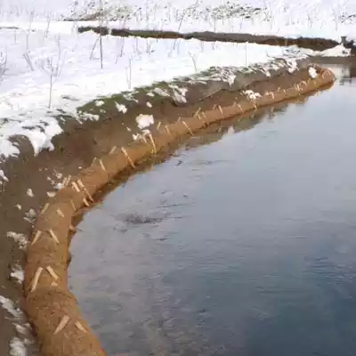 Coir logs installed along a snowy riverbank for erosion control and waterway protection.