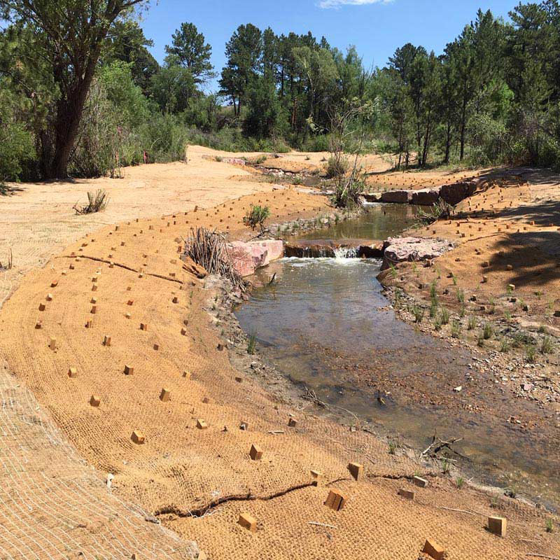 coir blankets Streambank restoration with coir mats securing the banks and promoting vegetation growth along a natural stream.