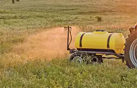Pasture sprayer with a yellow tank spraying a field